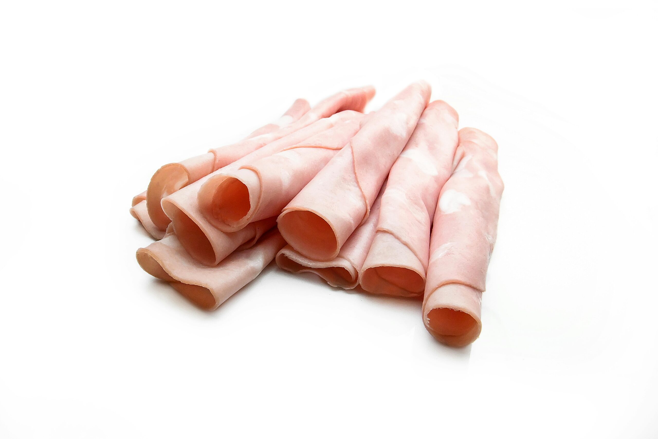 Close-up of delicious rolled ham slices on a white surface, perfect for finger food or sandwiches.